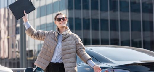 zena stoji pored automobila sa podignutom rukom u kojoj je vozacka dozvola