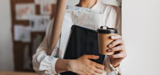 devojka sa kafom u jednoj ruci i fasciklom sa dokumentima u drugoj