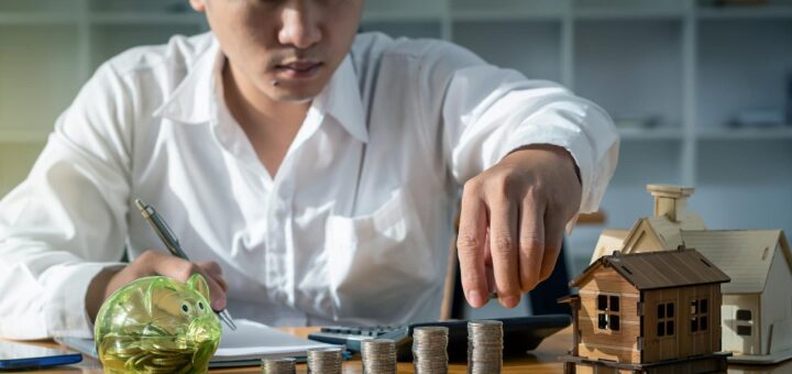 muskarac sa rasporedjenim metalnim novcicima i maketom kucice na stolu